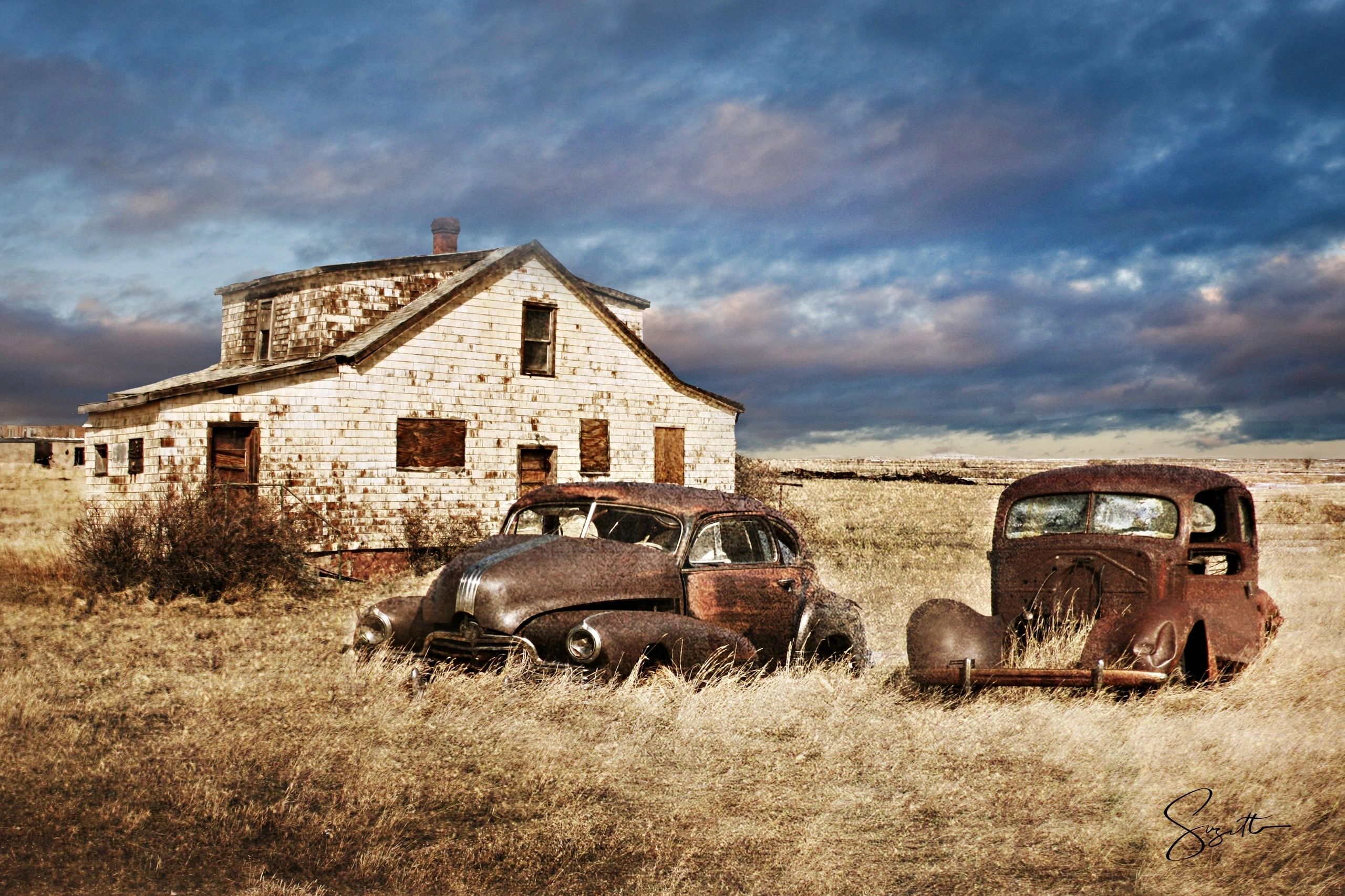 Abandoned house and cars in grassy field.